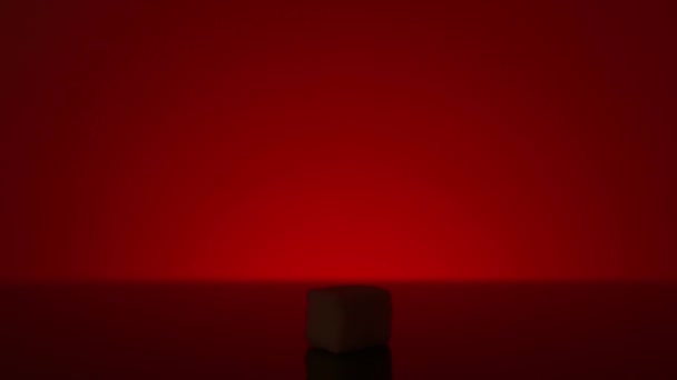 Single cube of sugar isolated on red background. Stock footage. Close up of a white sugar cube standing in the shadow with bright light shining then. — Stock Video