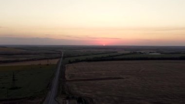 Tarımsal alanlardan ve tarımsal alanlardan geçen kırsal yolun havadan görünüşü. Görüntü. Tarım endüstrisi kavramı, ufka giden sonsuz yol ve güzel gün batımı..