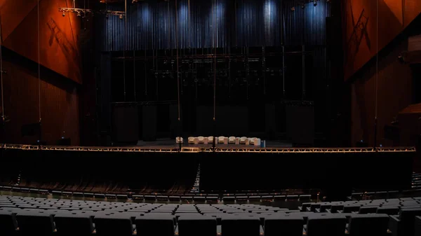 Large theatre hall with stage and balconies. Media. View from back rows of dark theater hall with dim lighting. Beautiful modern interior of theater hall with stage