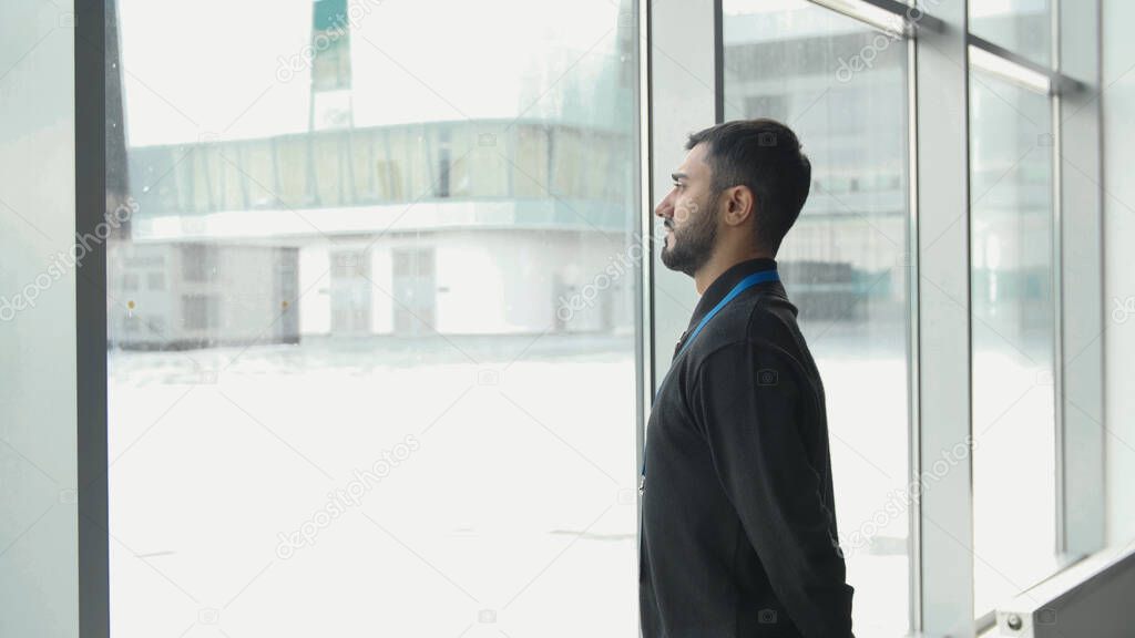 Office worker looks at snow. Media. Businessman frowns at falling snow through panoramic Windows. Office worker looks at snowfall outside window