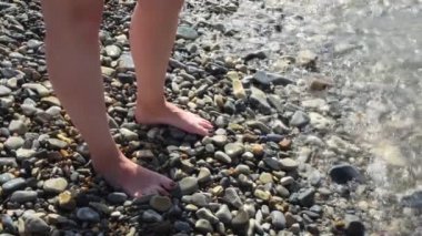 Güneşli bir yaz gününde kadın ayakları ılık deniz dalgalarıyla yıkanır. Kavram. Çakıl taşlı sahilde duran siyah tırnaklı güzel kadın ayaklarının manzarası..