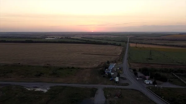 从空中俯瞰穿过农田和耕地的农村公路.镜头。土地工业的概念，通往地平线的无边无际的道路和美丽的日落. — 图库照片
