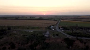 Tarımsal alanlardan ve tarımsal alanlardan geçen kırsal yolun havadan görünüşü. Görüntü. Tarım endüstrisi kavramı, ufka giden sonsuz yol ve güzel gün batımı..