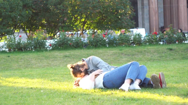 Felice giovane coppia sdraiata sull'erba al parco e godersi l'un l'altro. Concetto. Uomo baciare la sua ragazza sulla guancia e accarezzando i capelli, concetto di amore e tederness. — Foto Stock