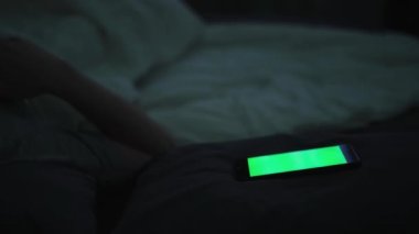 Genç adam sabahın erken saatlerinde yeşil ekranlı mobil çalar saatle uyanıyor. Kavram. Uykulu adam akıllı telefondan alarmlı saat sinyali duyduktan sonra uyanıyor.