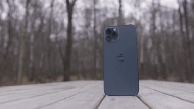 Tokyo, Japonya - 11.20.2020: Pasifik mavisi bir Apple Iphone 12 Pro Max 'e yakın çekim. Başla. Şehir parkındaki ahşap bir bankta dikey pozisyonda yeni akıllı telefon..