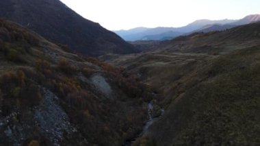 Arka planda nehir ve dağlar olan kurak sonbahar vadisi. Görüntü. Sarı yamaçlar boyunca akan kıvrımlı bir akarsuyun havadan görünüşü.