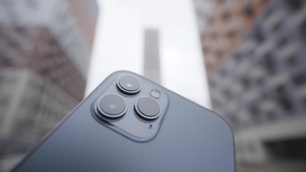 Koncept fotografie a natáčení videa. Akce. Detailní záběr super funkční kamery vysoké kvality na tmavě modrém smartphonu na rozmazaném pozadí obytných výškových budov. — Stock video