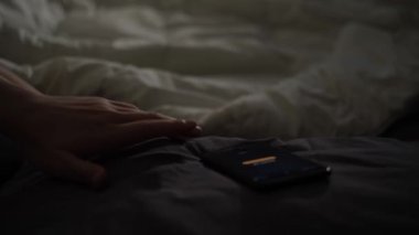 Evdeki cep telefonunda alarmla uyanan bir adam, rahat yatağında yatıyor. Kavram. Erkek el, karanlık bir yatak odasında uyandıktan sonra akıllı telefonunu alıyor..