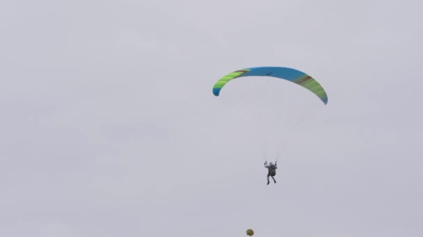 空にパラシュートを持つ男の下のビュー。行動だ。人は曇りの日にパラグライダーで空を飛ぶ。極端なスポーツとスカイダイビング — ストック動画
