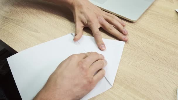 Руки роблять фігуру орігамі. Стокові кадри. Крупним планом чоловічі руки використовують білий аркуш паперу для виготовлення орігамі на дерев'яному тлі столу, концепція творчості . — стокове відео
