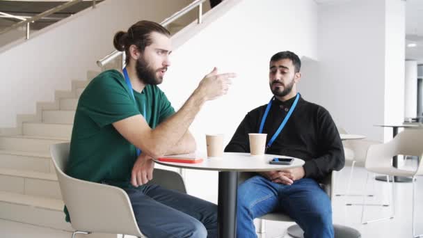 Két komoly fiatal kávézik és beszél az épületben fehér falakkal és lépcsőkkel. A média. Magabiztos üzleti partnerek ötleteket, tervezési projekteket és startupokat vitatnak meg. — Stock videók