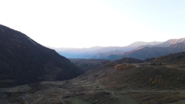 Sendero sinuoso en valle de montaña al atardecer en otoño. Filmación. Vista aérea de montañas, prados con hierba naranja, cielo azul y luz solar dorada. — Vídeos de Stock