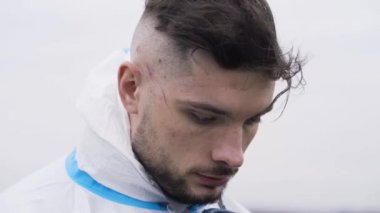 Sahanın arka planına bakan adam. Başla. Adam sahada duruyor ve bulutlu havada saçları rüzgarla savruluyor. Tulum giymiş bir adam.