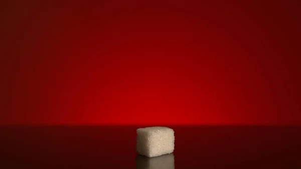 Single cube of sugar isolated on red background. Stock footage. Close up of a white sugar cube standing in the shadow with bright light shining then.