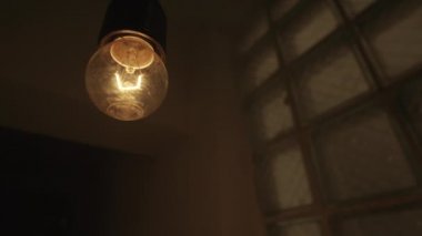 Sallanan bir ampulün sallanan alttaki görüntüsü. Stok görüntüleri. Bir binanın karanlık ve mistik atmosferinde yanıp sönen sarı bir ampulü kapat..