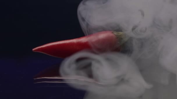 Vörös paprika füstölög. Készletfelvétel. Close up og piros forró hűvös paprika fekvő elszigetelt fekete háttér felhők füst, koncepció főzés élelmiszer. — Stock videók