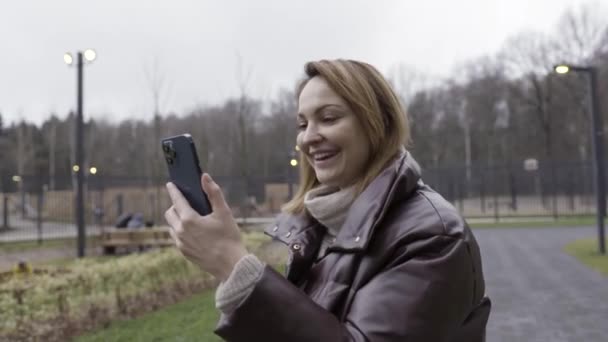 ウィーン、オーストリア- 11.20.2020:太平洋ブルーの新しい携帯電話を使用して女性。行動だ。新しいApple iPhone 12 Pro Maxを搭載したきれいな女性がビデオ電話をかけ、顔の時間を作り、手を振って — ストック動画