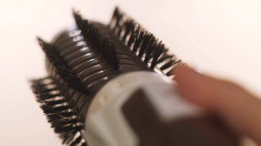 Beyaz arka planda saç düzleştirme için bir cilt fırçası tutan kız. Kavram. Kadın, her iki tarafa doğru dönen otomatik bir saç fırçasının tuşlarına basıyor..