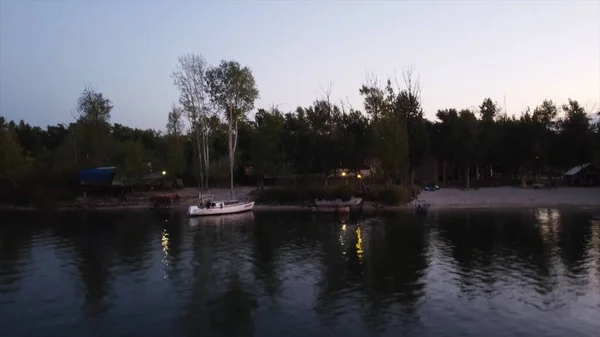 Schöner Fluss in einer ländlichen Gegend und ein Motorboot vor Anker. Verfilmung. Luftaufnahme eines kleinen Holzstegs und eines Bootes vor wachsenden Bäumen und Häusern, Sonnenuntergang in einem Dorf. — Stockfoto