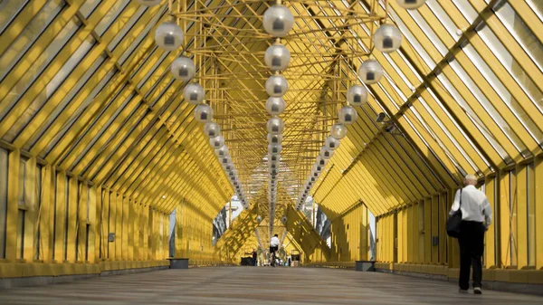 Folk går innanför gångbron i Moskva, Ryssland. Börja. Vy inuti Andrejevskij bro med ljusa gula metallbjälkar och hängande lyktor. — Stockfoto