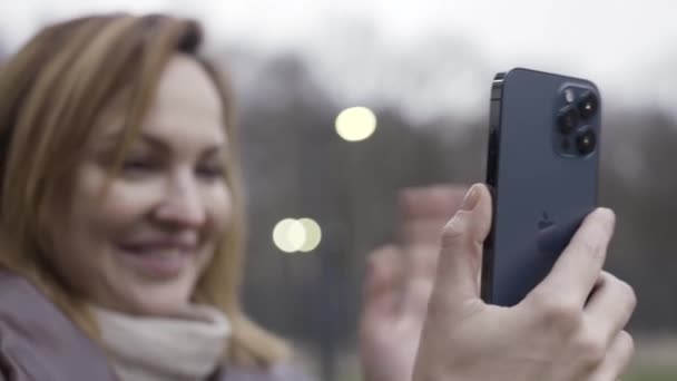 Wellington, New Zealand - 11.13.2020: μια νεαρή χαμογελαστή γυναίκα που έχει βιντεοκλήση και μιλάει με κάποιον, κοιτάζοντας το smartphone. Πάμε. Γυναικεία εκμετάλλευση Apple Iphone 12 pro max σε pacific μπλε χρώμα. — Αρχείο Βίντεο