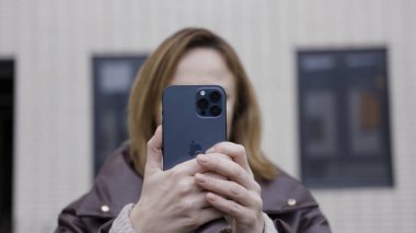 Riga, Letonya - 11.23.2020: Kadınlar yeni cihazıyla fotoğraf çekiyor veya video çekiyor. Başla. Yeni Apple Iphone 'u olan gülümseyen bir kadın. Maksimum 12 Pro..