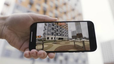 Akıllı telefon cihazını tutan bir elin detaylı görüntüsü ve çok katlı bir evin ve çocukların oyun parkının videosunu çekmek. Başla. Video çekimi için akıllı telefon kullanımını kapat.