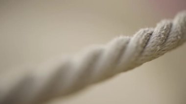 Bulanık bej arka planda bir ipe aşırı yakın çekim. Başla. Gerilmiş bej bir halatın makro görüntüsü. Kamera odağı ip boyunca yavaşça kayıyor..