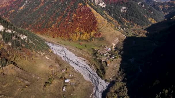 Luftfoto af en charmerende lille landsby beliggende nede i dalen nær skovklædte bakker. Optagelser. Flyver over bjergene dækket af farverige efterårstræer. – Stock-video