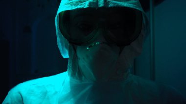 Tıbbi koruyucu giysili ve maskeli bir adam. Stok görüntüleri. Koronavirüs veya radyasyona karşı koruyucu giysi içinde manken. Tıbbi kıyafetli bir adamın üzerinde yanıp sönen ışık korku yaratır.