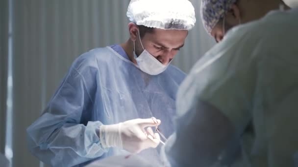 仕事中の男性外科医の閉鎖.行動だ。手術中に患者を見下ろし保護医療の制服を身に着けている集中医師の側のビュー,健康の概念. — ストック動画
