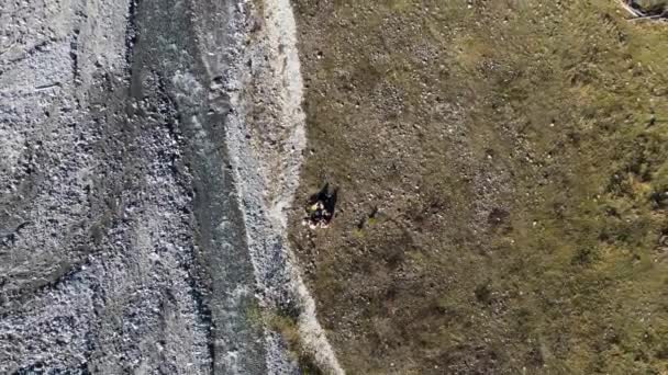 Conceito de turismo, caminhadas e estilo de vida ativo. Filmagem. Vista aérea superior de um grupo de jovens turistas bebendo chá chinês em um penhasco de montanha perto do rio pedregoso rápido. — Vídeo de Stock