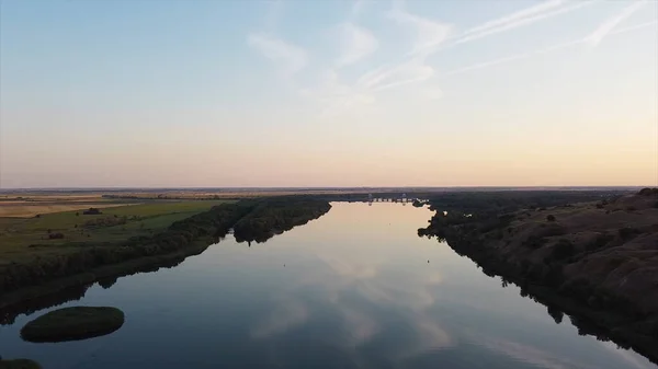 Beautiful river reflecting sky on background summer horizon. Footage. Surface of clear river reflects blue sky on background of green trees on banks. Beautiful panorama with blue river and green