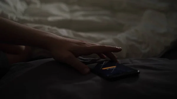 Mann wacht zu Hause mit Handy-Alarm auf und liegt in seinem warmen Bett. Konzept. Männliche Hand nimmt sein Smartphone nach dem Aufwachen zu Hause in einem dunklen Schlafzimmer. — Stockfoto