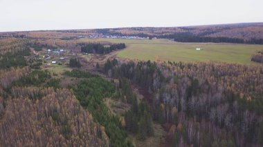 Sonsuz bir sonbahar ormanı ve bir köyün manzaralı panoramik manzarası. Şarjör. Kırsal alan, karışık orman, kırsal bir köyün geleneksel evleri, yaşamak için ekolojik bir yer..