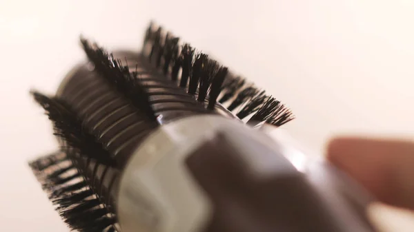 Chica sosteniendo un volumebrush para alisar el cabello aislado sobre fondo blanco. Concepto. Pulsando los botones de la mano de una mujer de un cepillo de pelo automático que está girando en ambos lados. — Foto de Stock