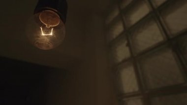 Sallanan bir ampulün sallanan alttaki görüntüsü. Stok görüntüleri. Bir binanın karanlık ve mistik atmosferinde yanıp sönen sarı bir ampulü kapat..