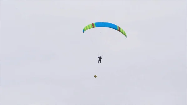Vue du bas de l'homme avec parachute dans le ciel. L'action. La personne vole dans le ciel sur le parapente par temps nuageux. Sports extrêmes et parachutisme — Photo