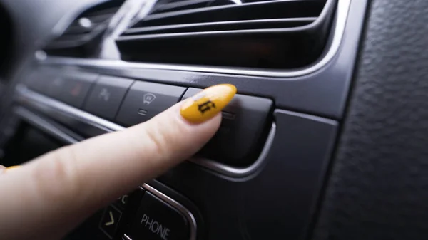 Close-up of woman pressing button on car panel. Action. Woman with manicure presses seat heating button. Button for seat heating in car