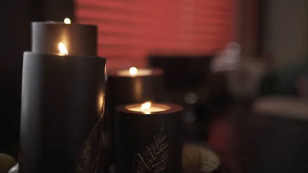 Close up of big dark burning candles creating romantic and calm atmosphere. Action. Details and decorations of room interior, chocolate aroma candles on the background of red blinds. — Stock Photo, Image