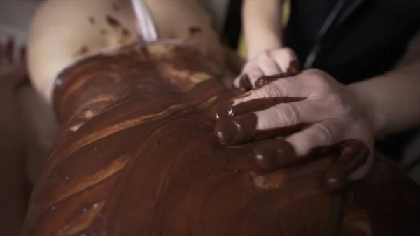 Belle femme se faire masser au chocolat dans le salon de spa. L'action. Gros plan des mains masculines massant le dos féminin avec du chocolat chaud fondu, concept de procédure de beauté. — Photo