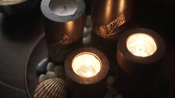 在木制桌子的黑色背景上，近距离观看点燃蜡烛的情景。行动。在盘子里放着深褐色的蜡烛、装饰性的石头和海贝壳的亲密而平静的气氛. — 图库照片