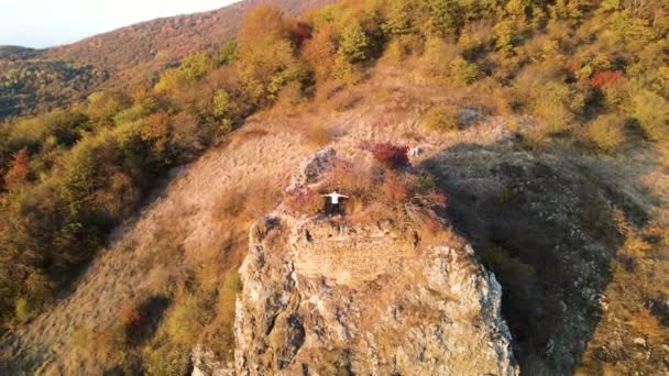 Man standing on mountain ledge. Footage. Top view of man with arms outstretched on rock. Free man is happy to climb mountain ledge with beautiful view. Ascent to mountain on Sunny autumn day — Stock Video