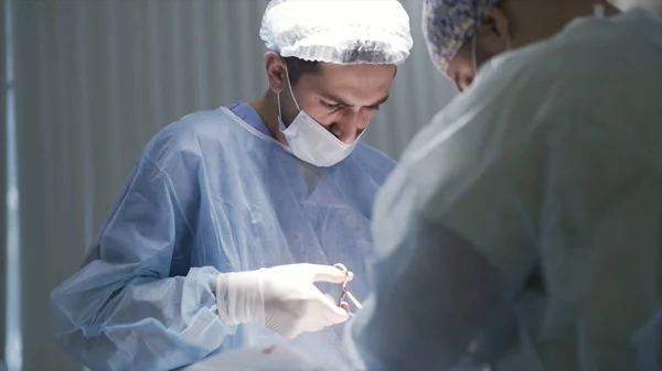 Közelkép a férfi sebészekről a munkahelyen. Felvétel. Oldalnézet koncentrált orvosok néz le a beteg műtét közben, és visel védő orvosi egyenruha, az egészség fogalma. — Stock Fotó