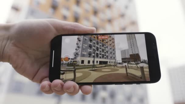 Detailweergave van een hand die een smartphone-apparaat vasthoudt en het maken van een video van een huis met meerdere verdiepingen en een speeltuin voor kinderen. Actie. Close-up van het gebruik van smartphone voor video-opnamen. — Stockvideo