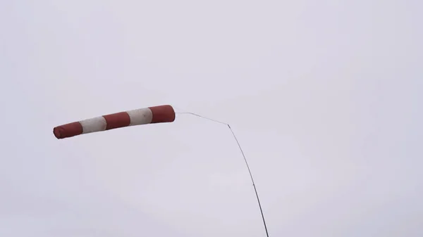 Meia de vento soprada pelo vento no fundo do céu nublado, cinzento e pesado. Acção. Meteorologia abandonada windsock de cor vermelha e branca balançando no vento forte. — Fotografia de Stock