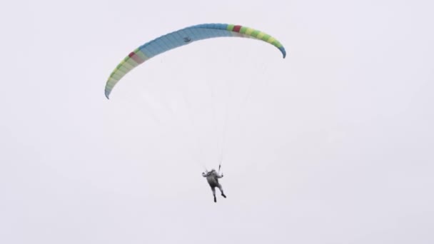 Achteraanzicht van een parachutist die rondcirkelt in de lucht met een vleugelparachute. Actie. Professionele lucht duiker trekken de sling om de parachute te controleren tijdens het vliegen op grijze bewolkte lucht achtergrond. — Stockvideo