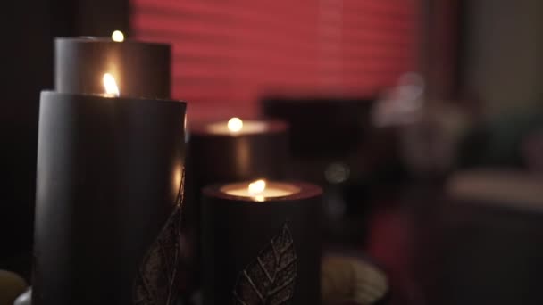 Close up of big dark burning candles creating romantic and calm atmosphere. Action. Details and decorations of room interior, chocolate aroma candles on the background of red blinds. — Stock Video