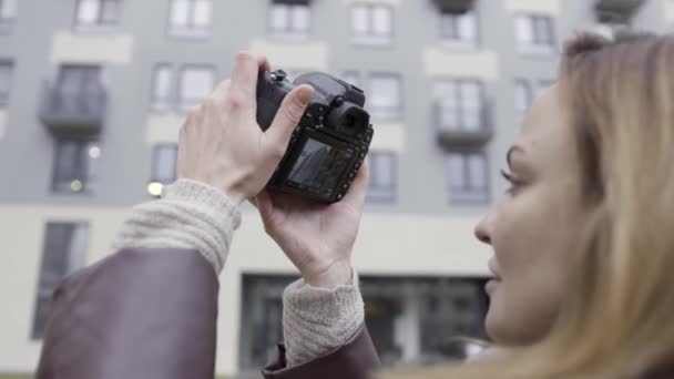 Ontdek nieuwe plekken, zijaanzicht van een fotograaf aan het werk buiten die foto 's maakt van een nieuw hoogbouw. Actie. blond mooi fotograaf vrouw met een professionele camera in haar handen nemen — Stockvideo